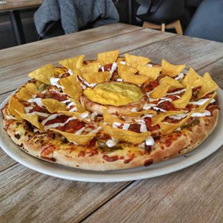 A beef-cheddar pizza with tons of nachos, sauces and salsa on it ????????????